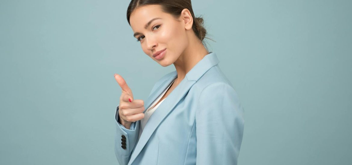 A young woman in a blue suit exhibits confidence with a relaxed pose against a blue background.