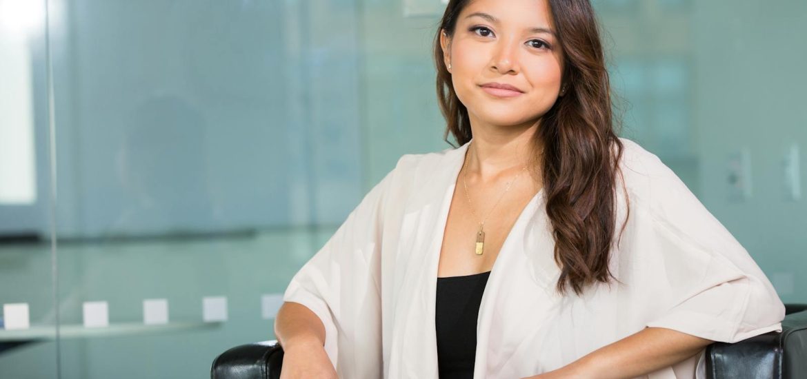 A professional Asian businesswoman sitting confidently in a modern office setting.