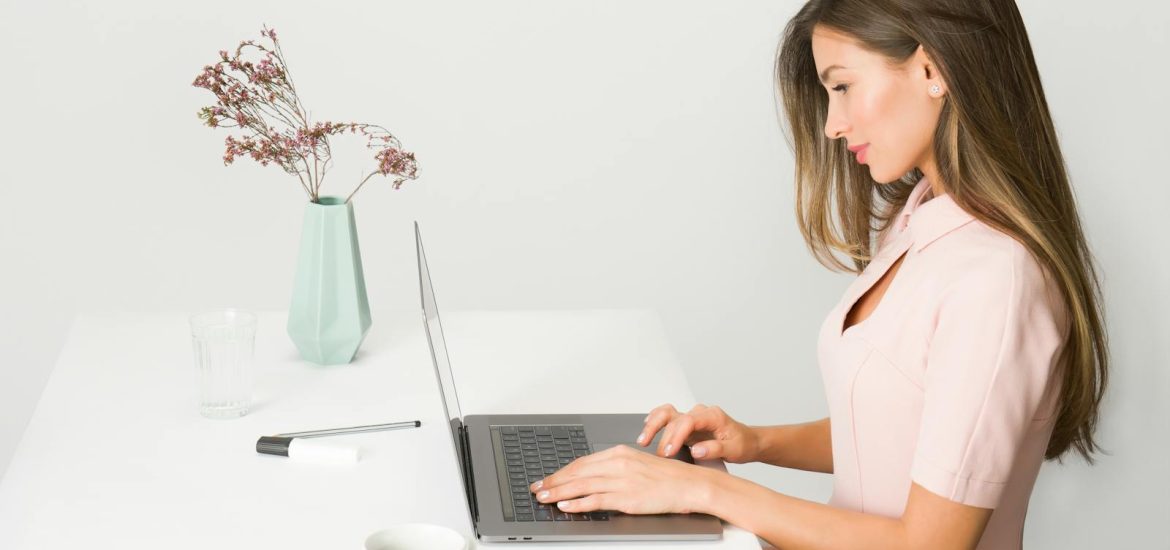 A woman in a pink dress working on a laptop at a modern, minimalist desk.