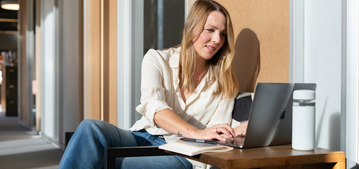 woman in white long sleeve shirt and blue denim jeans sitting on brown wooden table using